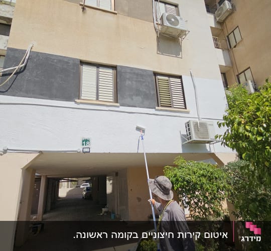 אדם צובע קיר חיצוני של בניין עם רולר ארוך